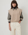 Sessun Fabinino beige sleeveless jumper layered over a gray shirt, styled with white pants for a relaxed look.