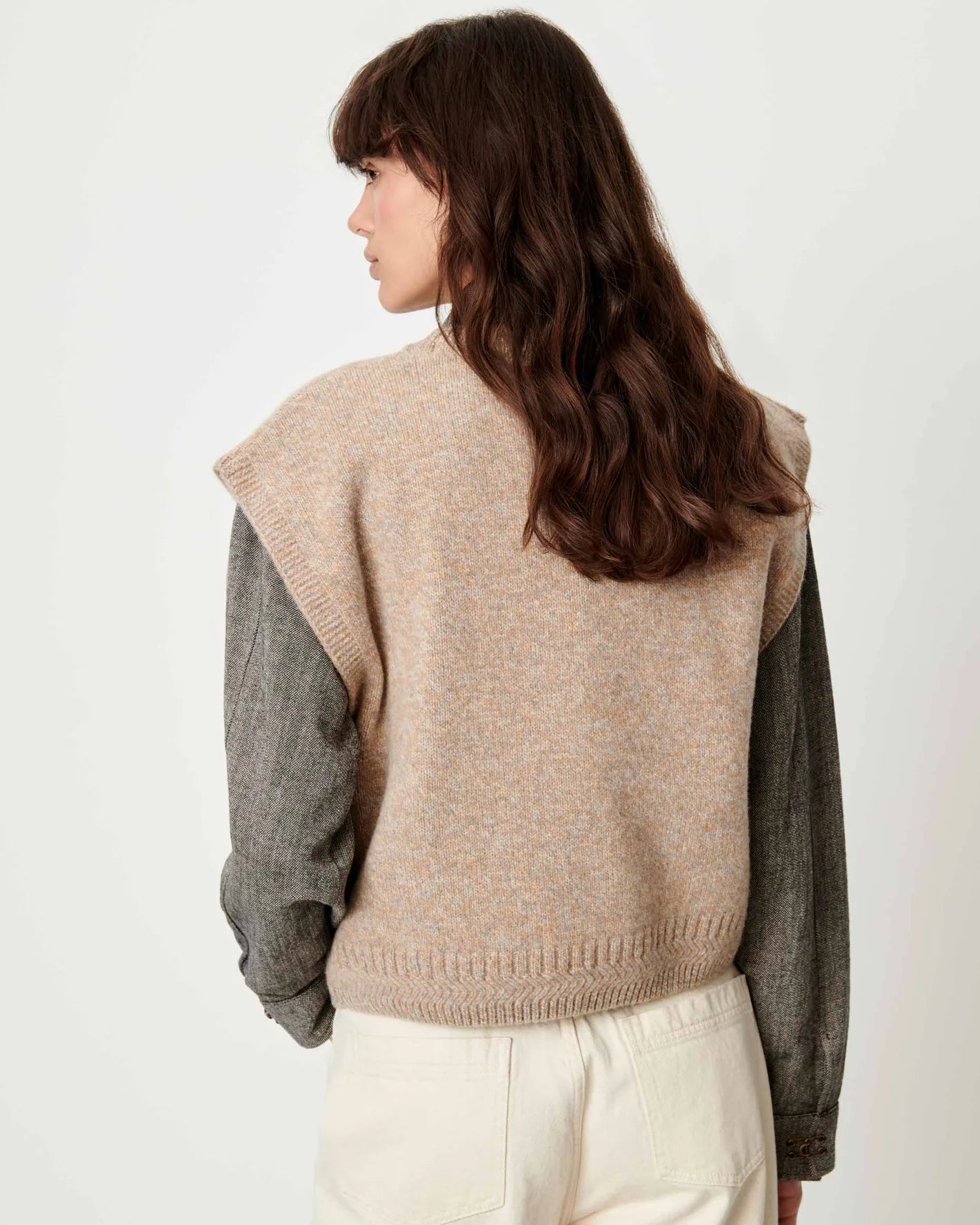 Beige Sessun Fabinino Sleeveless Jumper over gray shirt, shown from the back, wavy brown hair visible.