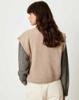 Beige Sessun Fabinino Sleeveless Jumper over gray shirt, shown from the back, wavy brown hair visible.