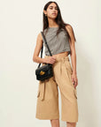 A woman with long, straight hair stands against a plain background wearing Sessun Marco Bermuda Shorts, a checkered sleeveless crop top, and a black crossbody bag with gold accent.