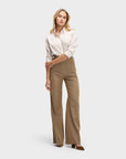 A woman stands against a plain background wearing the Weekend Shirt by Sarah Alexandra, LLC, a neutral striped top tucked into high-waisted, wide-leg brown trousers with front pockets and brown heels.