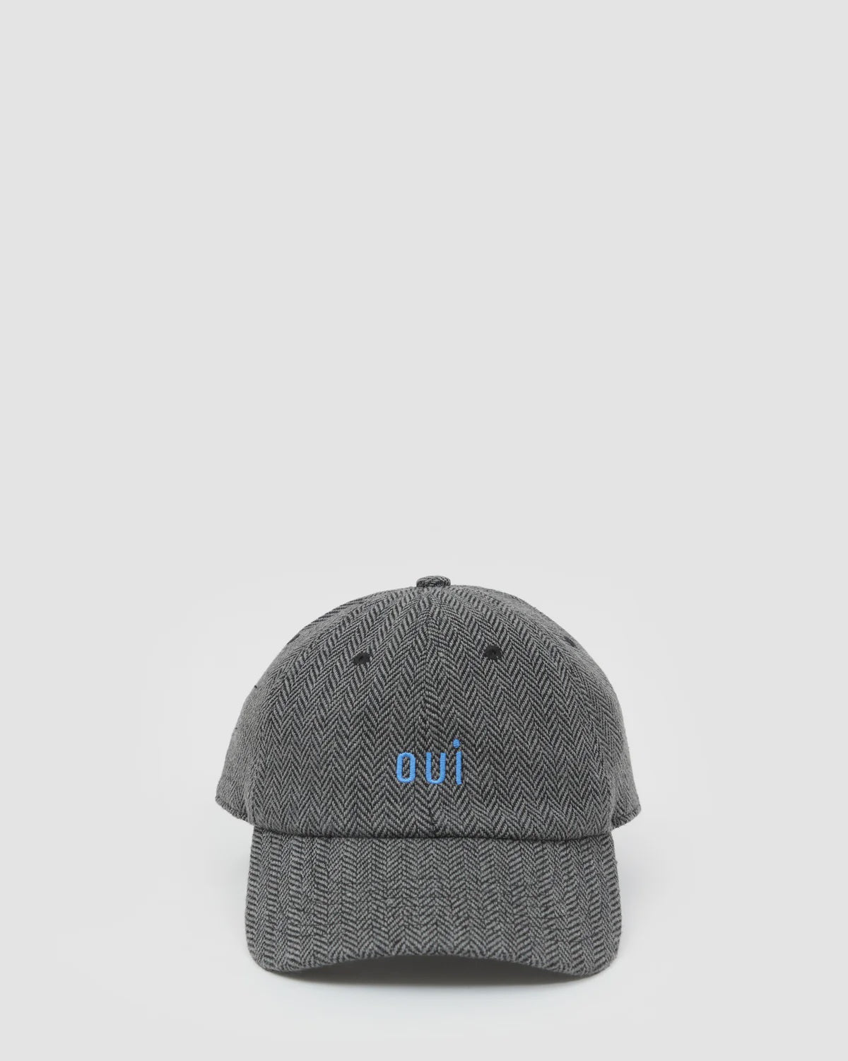 Gray herringbone wool baseball hat with small blue oui text on front by Clare Vivier shown on a plain background.