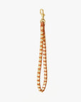 The Clare Vivier Wristlet is a brown Italian leather accessory featuring gold metal studs and clasp, perfect as a keychain or accent piece. Shown laid flat on a white background.