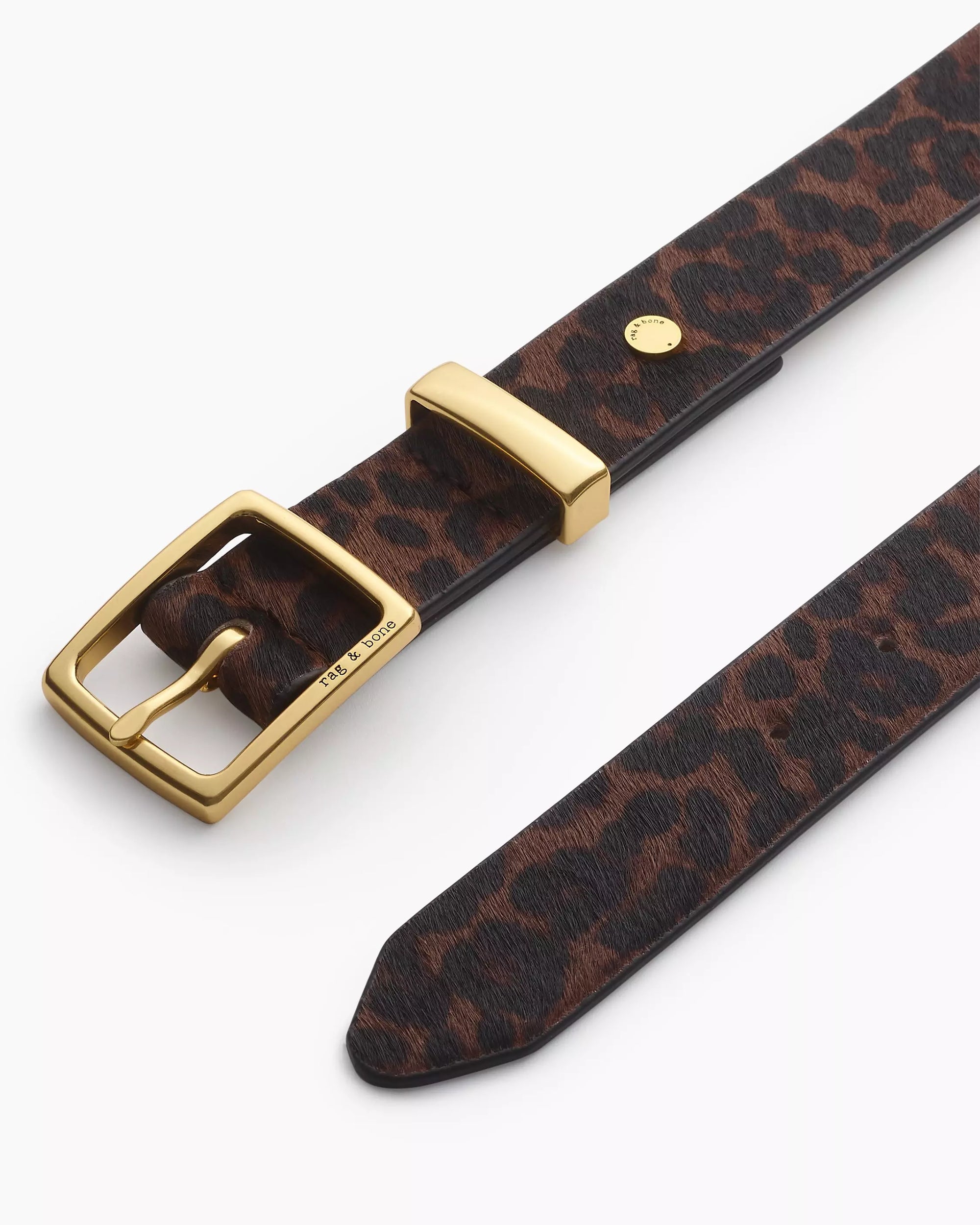 A close-up of the Rag & Bone X Boyfriend Belt, a menswear-inspired calf hair accessory with a gold buckle, pointed end, and rich brown and black leopard print.