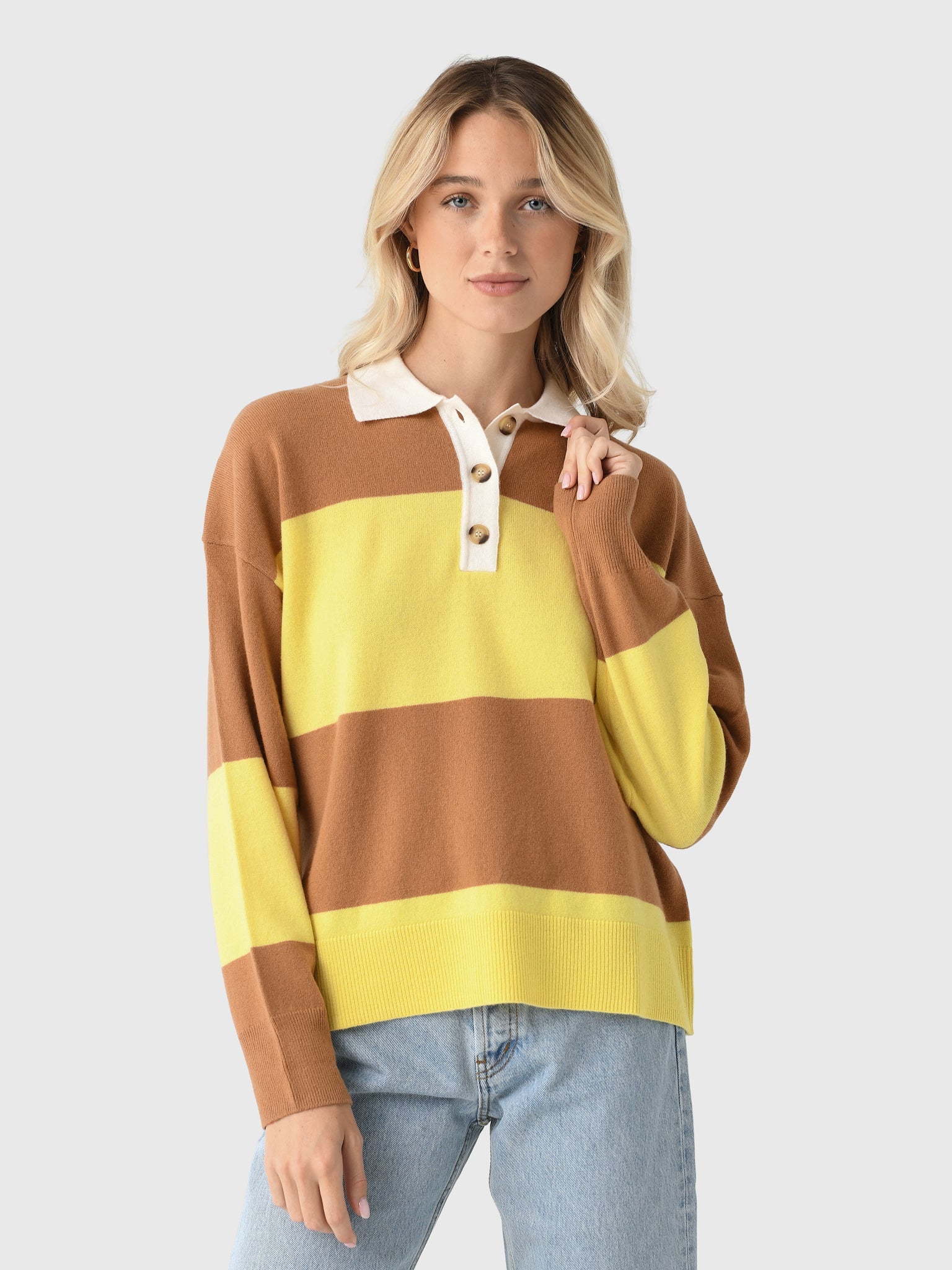 A blonde woman wears the Xirena Braxton Sweater—brown and yellow stripes with a white collar—styled with blue jeans, against a light background.