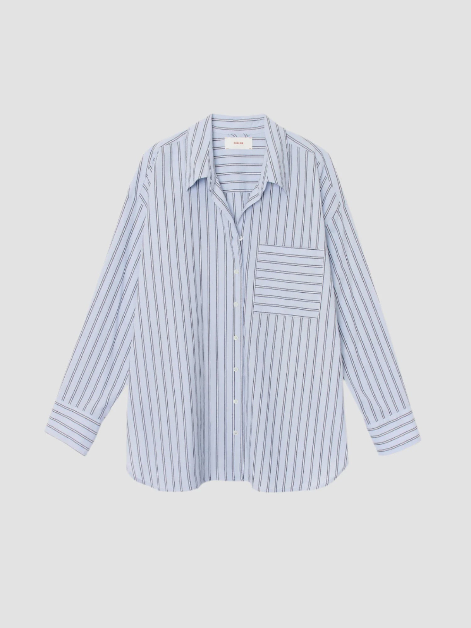 The Sydney Shirt by Xirena is an oversized light blue cotton poplin button-down with thin vertical navy stripes and a large chest pocket, shown against a plain white background.