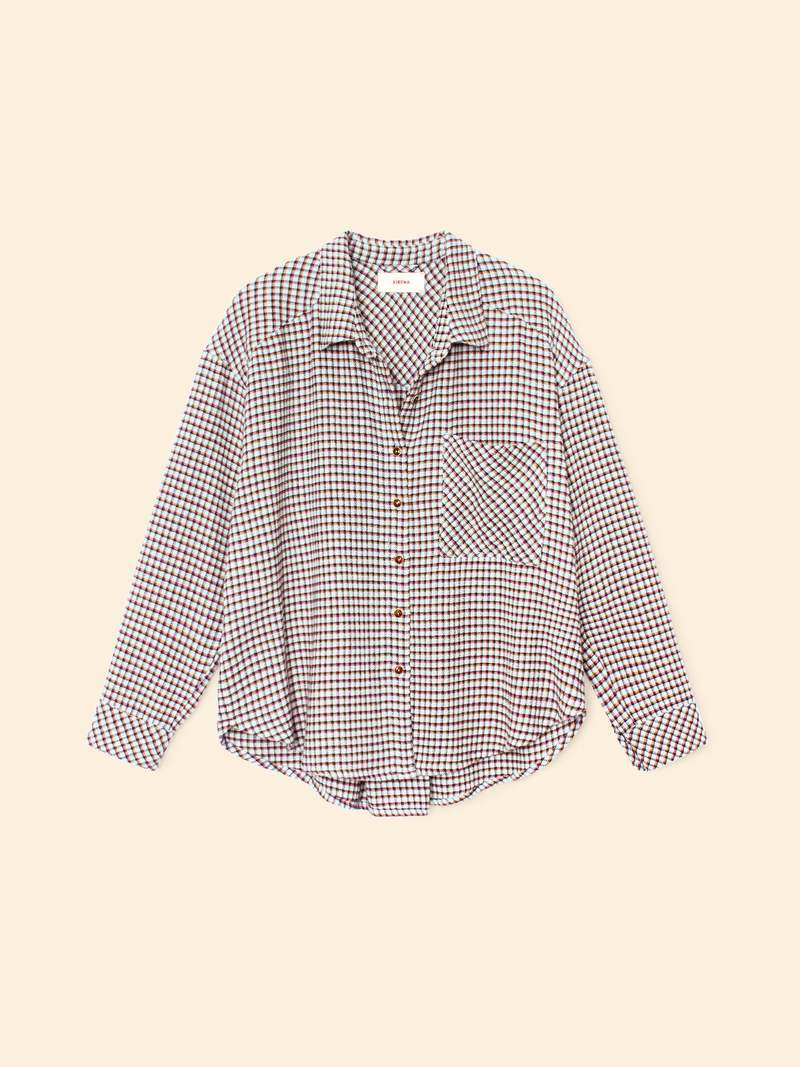 The Xirena Jordy Shirt S25 is a relaxed-fit cotton button-front shirt with long sleeves, chest pocket, and a small brown-and-white checkered pattern, shown on a plain beige background.