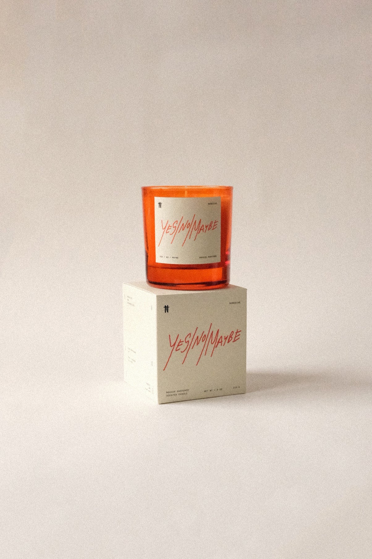 The Nosedive Candle by Faire, a vegan orange soy candle labeled "YES/NO/MAYBE," sits on its matching white box against a light background. Enjoy its rich Smoky Woody scent, inspired by Mixtape 1999.