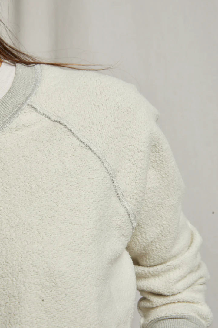 Close-up of a person wearing the Perfectwhitetee Ziggy Reverse LS Sweatshirt in off-white cotton fleece with a light gray collar and seam details; only the shoulder, part of the arm, and some hair show against a neutral background.