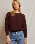 A person with long blonde hair wears the Ziggy Inside Out Longsleeve Crewneck Sweatshirt by Perfectwhitetee, paired with blue jeans, standing against a plain, light-colored background. They have a neutral expression and one hand in their pocket.