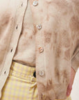 A close-up of a person wearing the Batik Cardigan by Jumper 1 2 3 4/CR2 over a matching top, styled with high-waisted yellow and white gingham pants, with their hand resting on their hip.