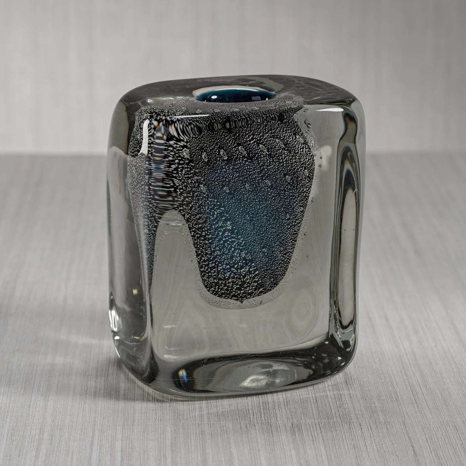 The Zodax Crystal Bloom Vase is a square, clear glass vase with rounded edges, a blue-tinted center, and textured bubbles inside—ideal as premium home décor on a light gray surface with a subtle background.
