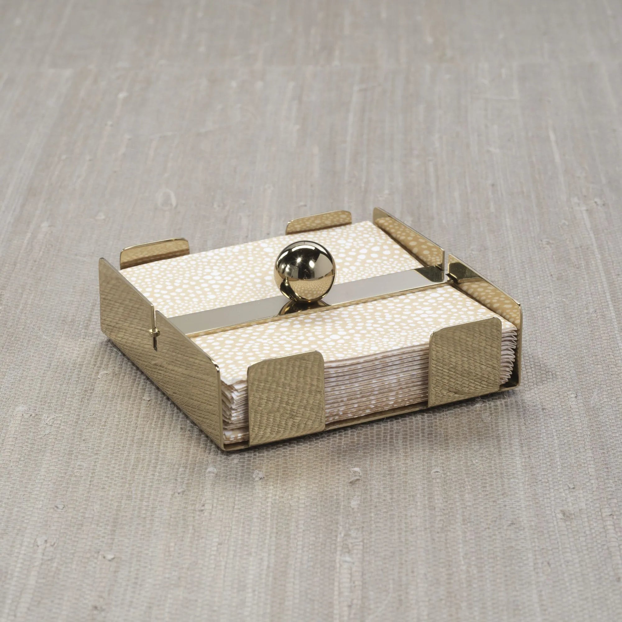 The Zodax Cocktail Napkin Holder Gold features a central horizontal bar with a round gold knob and holds stacked napkins elegantly on a light textured surface—an ideal accessory for any setting.