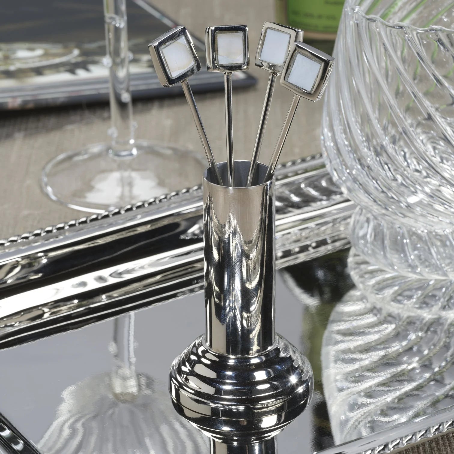 The Zodax Cocktail Picks S4 features four silver picks with square white tops in a matching holder, elegantly displayed on a reflective tray—an ideal sleek accent for your modern barware collection.