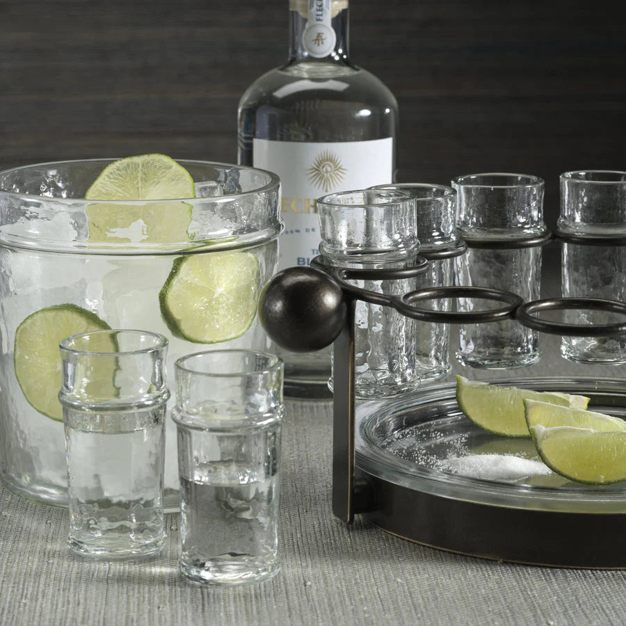 The Zodax Ten Shot Tequila Set w/Ice Bucket features a clear liquor bottle, ice bucket, shot glasses, a pitcher with ice and lime slices, lime wedges on a tray, and a salt dish arranged on a gray surface.