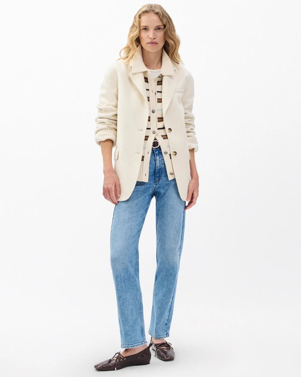A woman with wavy blonde hair wears the Rag & Bone zoe wool blazer over a striped sweater, light blue jeans, and dark brown loafers, standing against a plain white background.