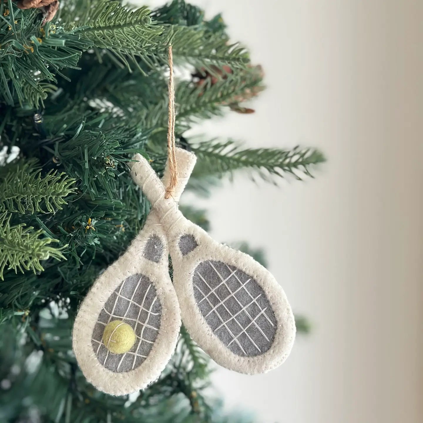 Faire’s Felted Ornament features two crossed tennis rackets and a small yellow ball, making it the perfect sporty touch for your Christmas tree.