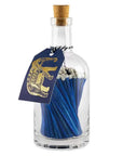 The Faire Glass Bottle Matches offer sustainable home living with blue matches and white tips in a cork-sealed glass bottle. A blue tag featuring a gold elephant is attached to the neck with black and white string, all in plastic-free packaging.