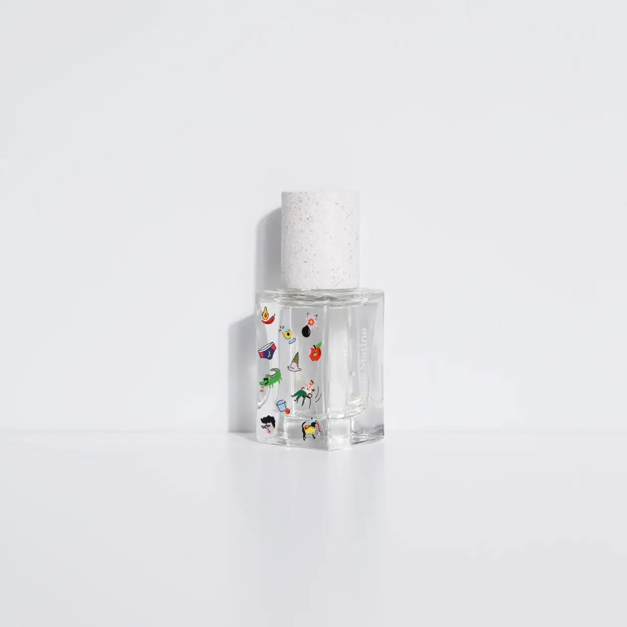 The Maison Matine Perfume by Faire features a clear glass bottle with a white speckled cap, adorned with colorful stickers of objects and animals, and hints at notes of bergamot and musk, displayed on a plain white background.