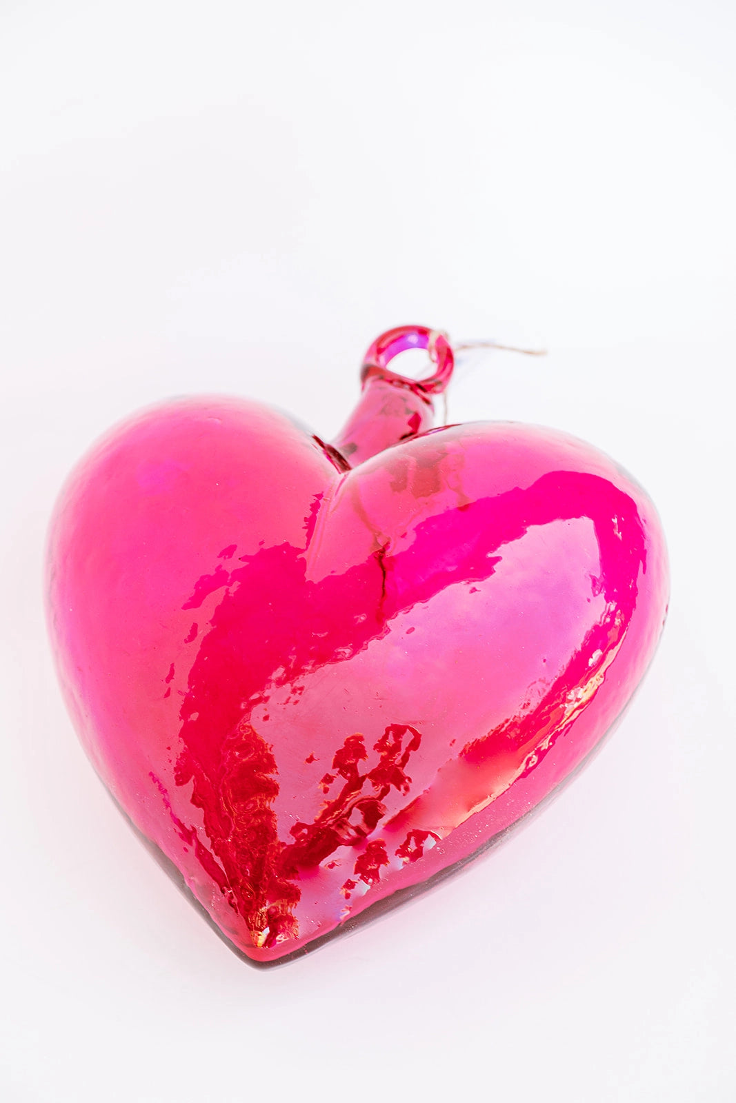 The Faire Glass Heart Medium, a vibrant red handcrafted Blown Glass ornament with a glossy finish, embodies Mexican tradition. It gleams against a white background and includes a small loop at the top for hanging.