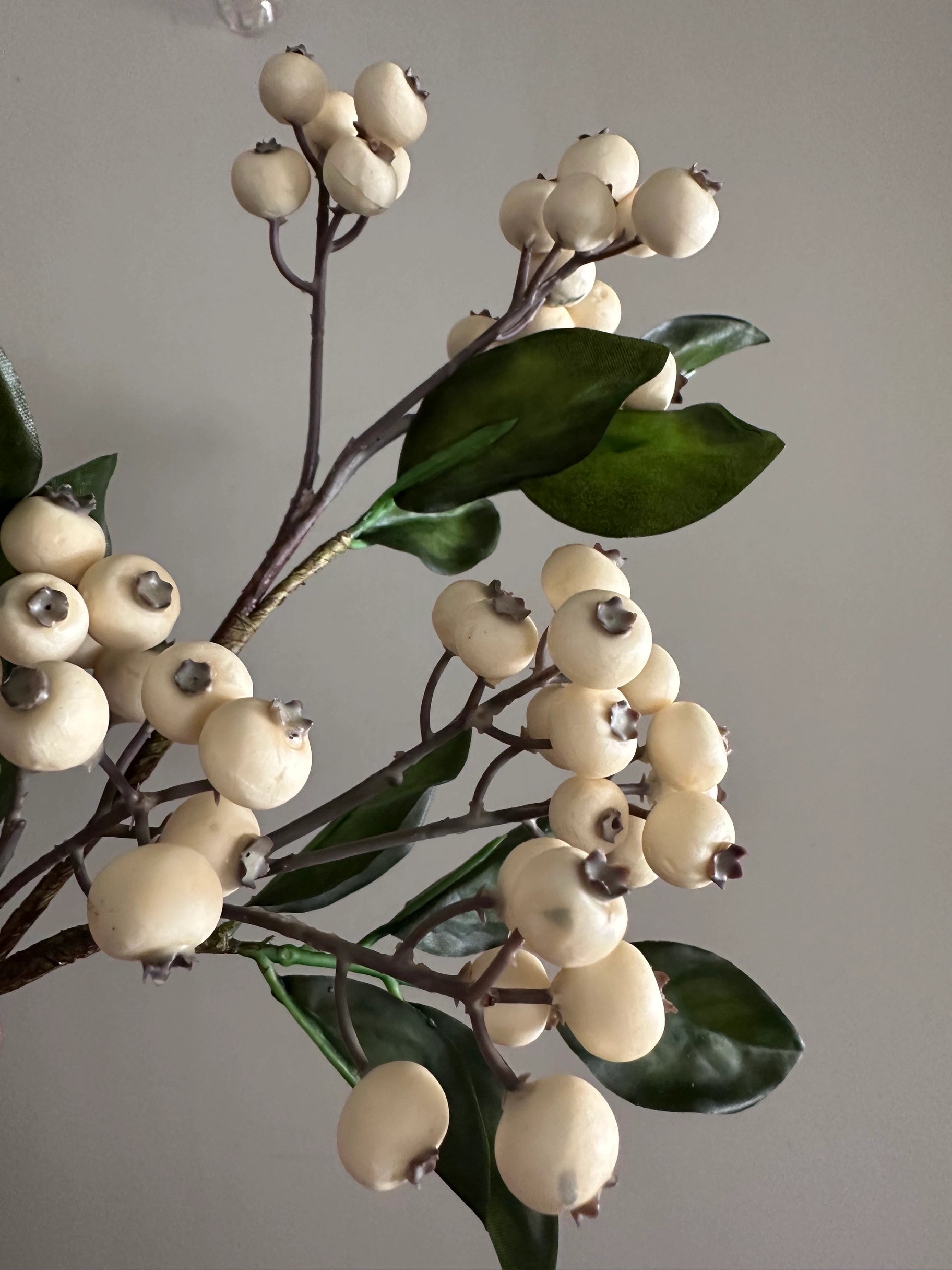 Faux cream berry and green leaf pick by Faire, 15-inch stem against a gray background.