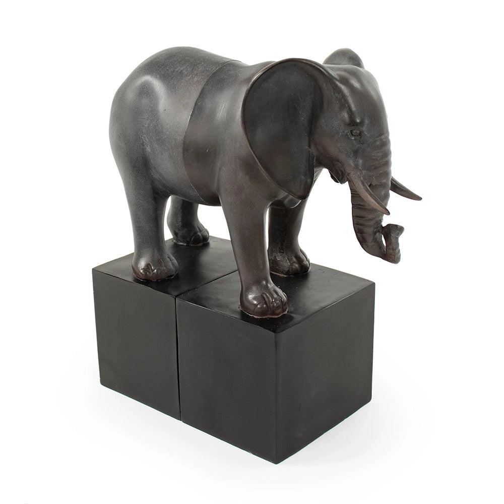 The Zentique Elephant Bookends feature a dark bronze elephant standing with one foot on each of two black rectangular blocks, making them a unique and stylish decorative bookend set.