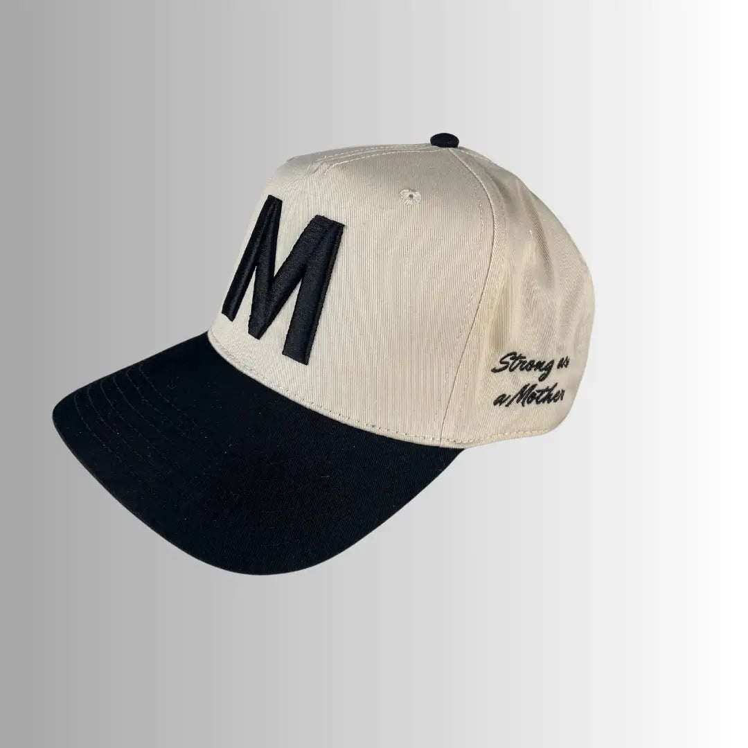 The M Hat by Faire features beige and black embroidery, a bold black "M" on the front, and "Strong as a Mother" stitched on the side, shown against a light gray gradient background.