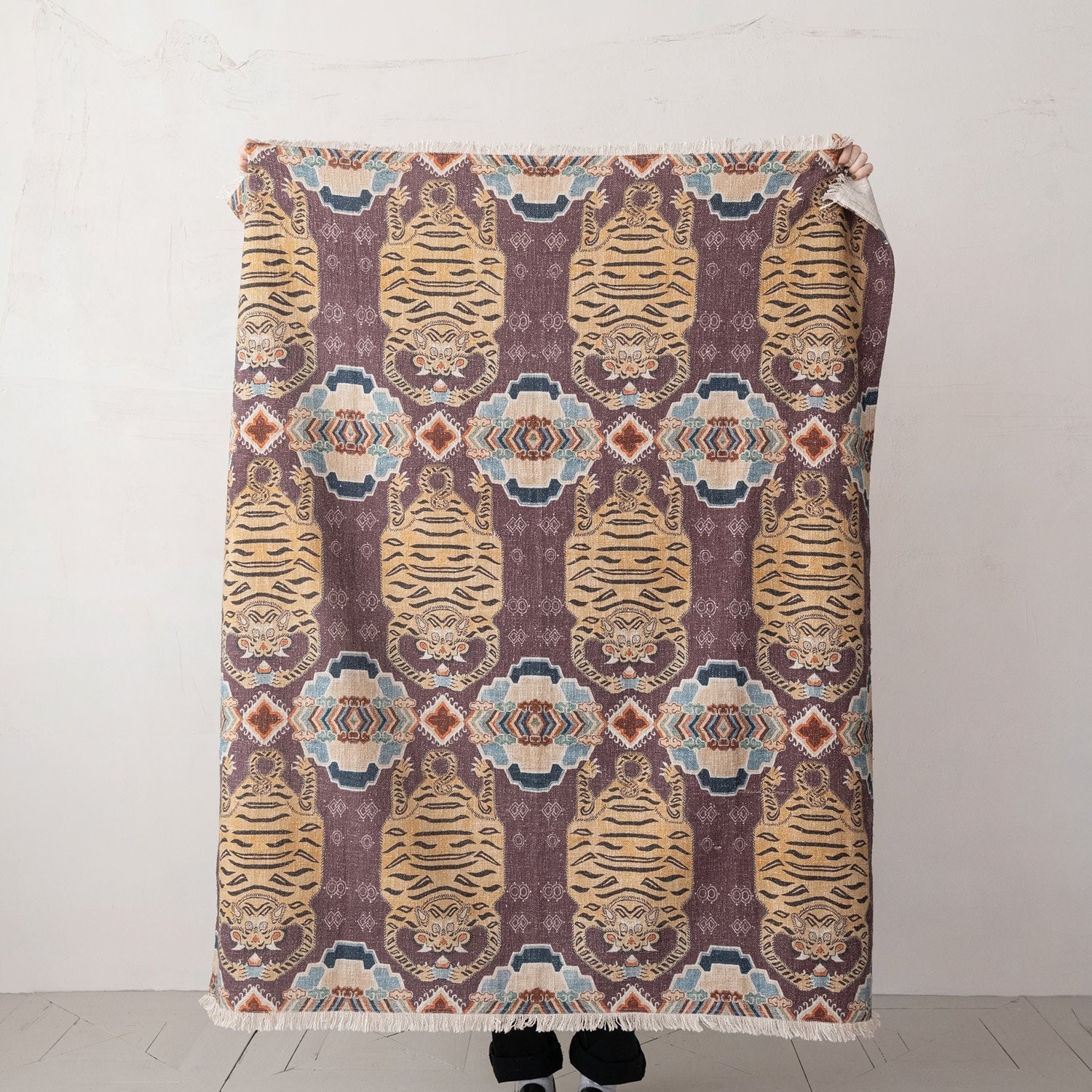 A person stands behind the Bloomingville Cotton Throw / Tibetan Tigers, featuring stylized tiger faces and geometric shapes—only their feet show below this boho Cotton Slub blanket.