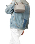 Wearing a patchwork denim jacket and white pants, the person carries a Jerome Dreyfuss Ben Small Bucket, a gray calfskin handbag with a sleek leather strap. The individual faces away, showcasing the back of their outfit and bag.