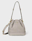 The Ben Small Bucket by Jerome Dreyfuss is a light gray calfskin bag with gold-tone hardware and an adjustable strap, featuring seam details, a drawstring closure, and a minimalist design on a white background.