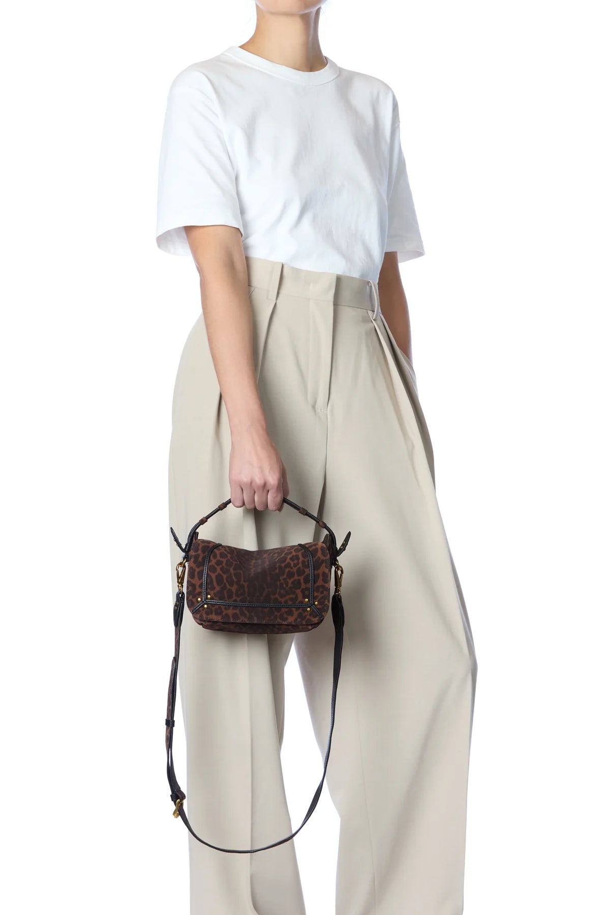 A person wearing a white t-shirt and beige high-waisted trousers holds the Pepito Small Bag by Jerome Dreyfuss. Made in Italy, this chic quilted leather shoulder bag features a striking leopard print, standing out against the plain white background.