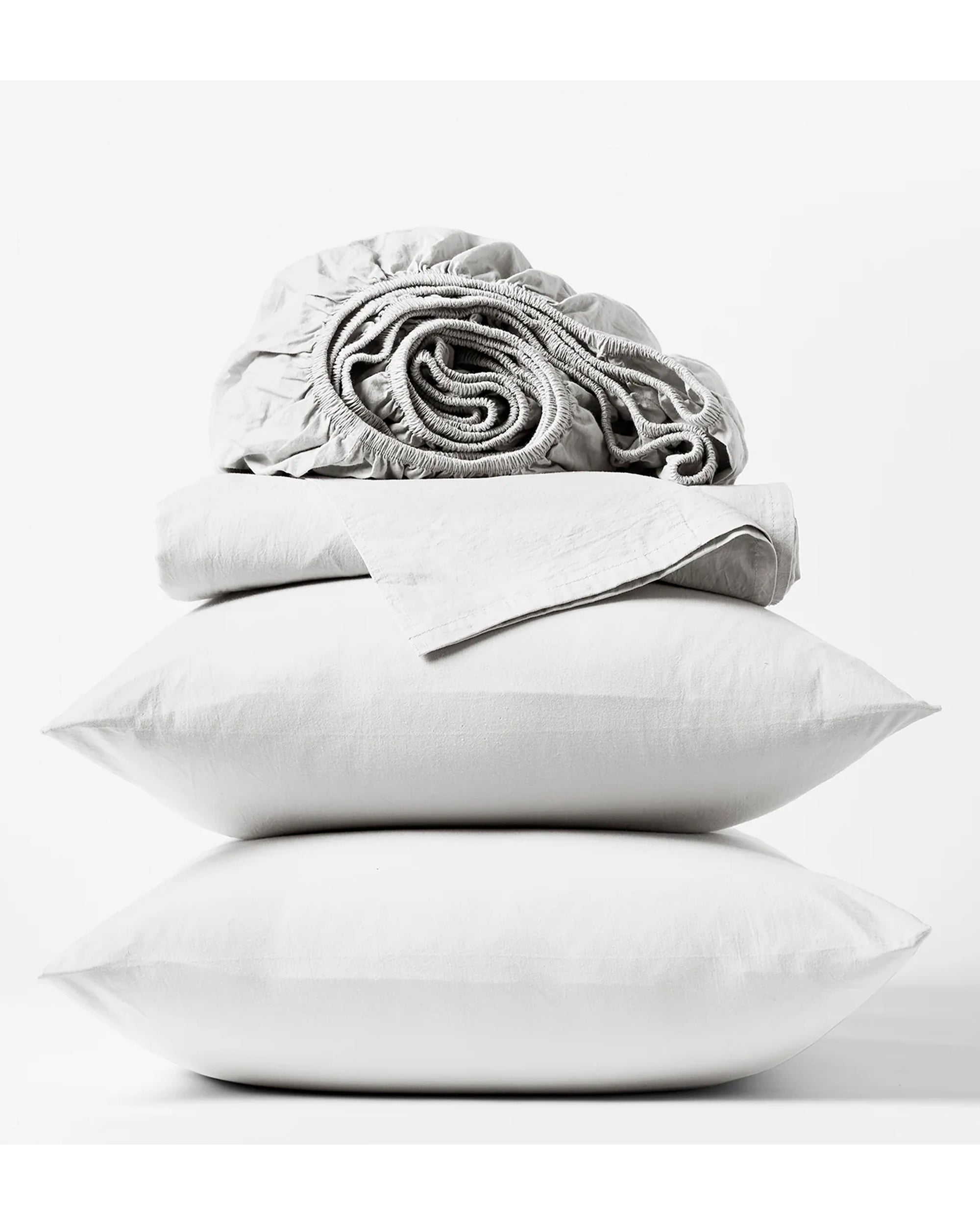 A stack of two white pillows topped with the Coyuchi Inc Org. Crinkled Percale Sheet Set in Alpine White King, all crafted from GOTS Certified organic cotton, arranged neatly against a plain white background.