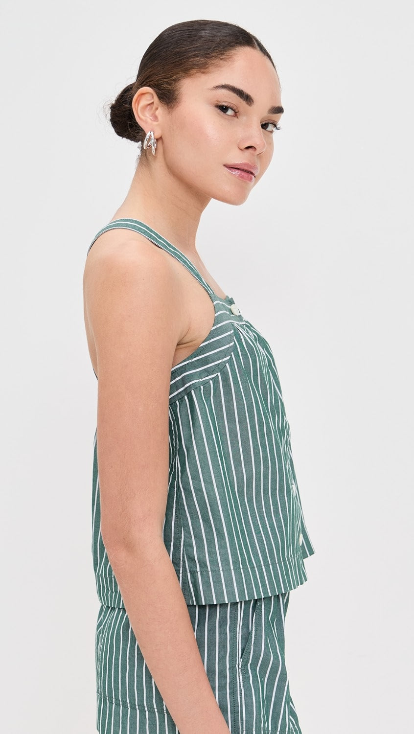 A woman with dark hair in a low bun poses sideways against a white background, wearing the Alex Mill Leah Top In Stripes—a green and white vertically striped sleeveless top in lightweight fabric.