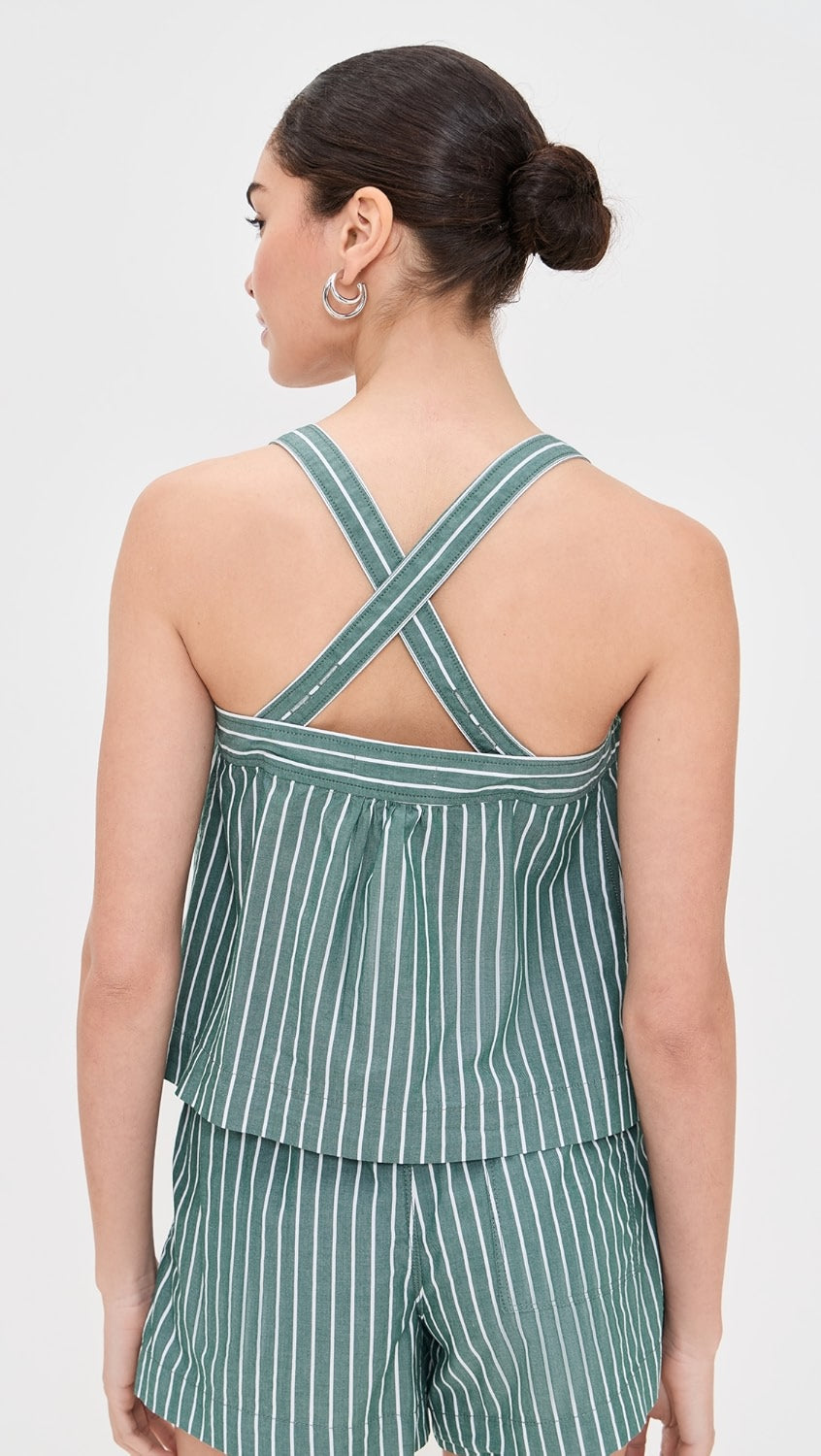 A woman with dark hair in a bun is seen from behind wearing the Alex Mill Leah Top In Stripes, a green and white sleeveless top with crossed back straps, paired with matching shorts against a plain background.