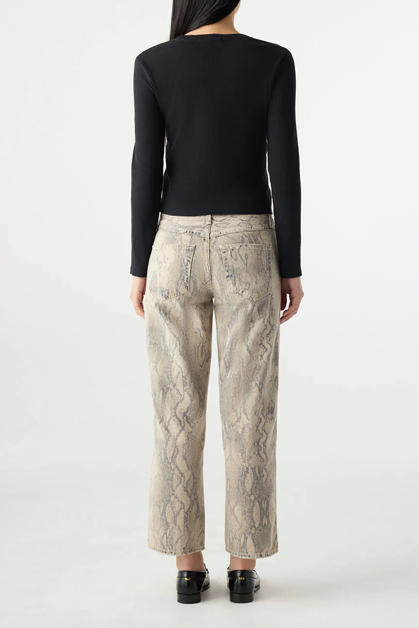 A person with long dark hair, wearing a black long-sleeve top and AMO Denim Billie Pants in relaxed-fit beige snake-print, stands facing away from the camera against a plain white background.