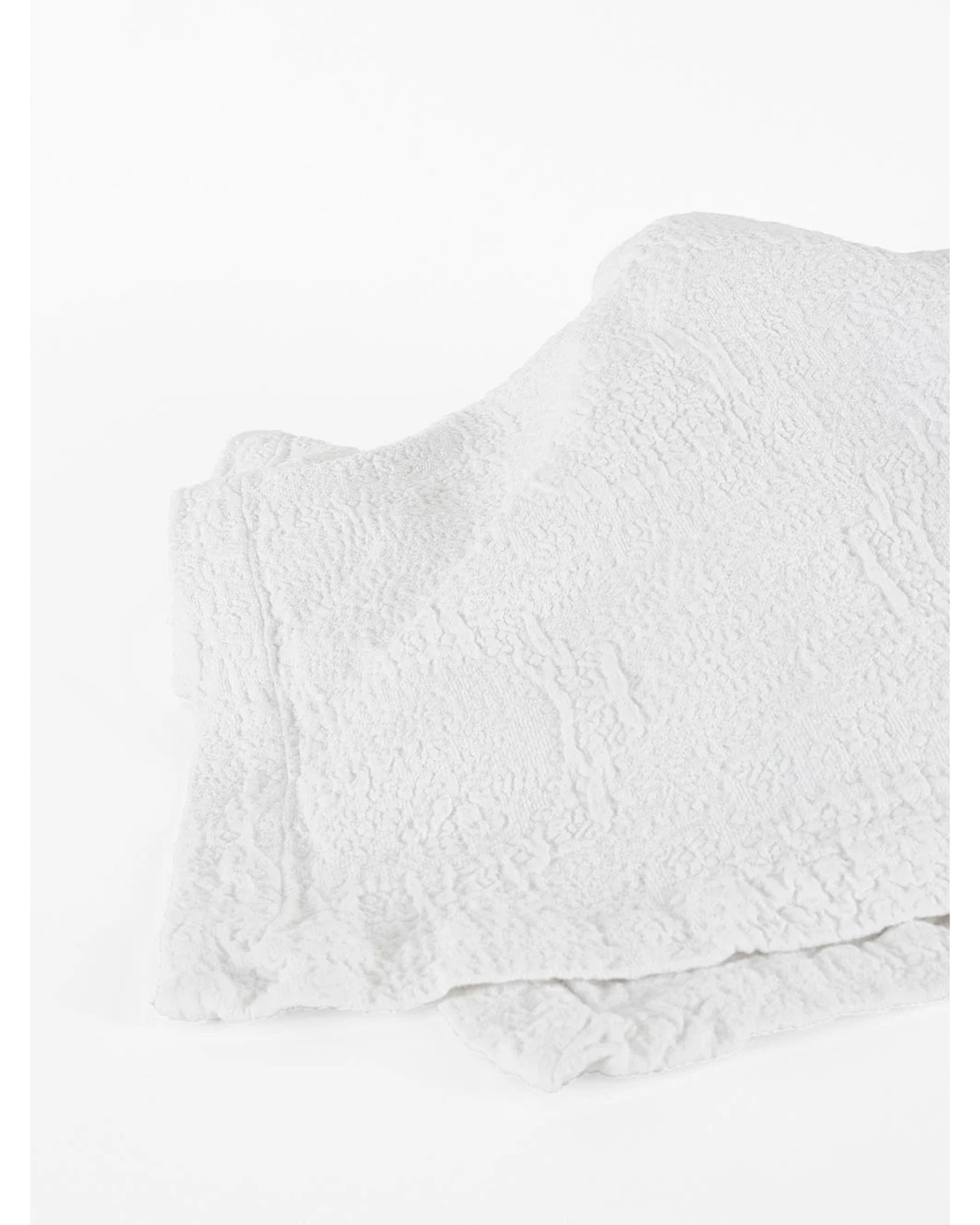 Two folded Antik Matelasse Coverlets by Matteo, featuring a subtle crinkled jacquard weave, rest on a white surface, adding depth and texture.
