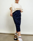 A woman wearing sunglasses, a loose beige t-shirt, the Aquarius Cocktail CAMO LE Pencil Slim Skirt, white socks, and brown sandals stands confidently against a plain background.