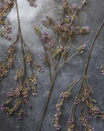 The Berry Branch Lilac by Abigail Ahern features delicate brown branches with small lilac and green artificial berries, arranged on a dark textured surface for a natural, artistic display.