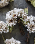 Several small hand-painted fabric bouquets from Abigail Ahern's AA-N4-001 Garden Bouquet, featuring dark centers and green leaves, are tied with twine and arranged on a textured dark gray surface.