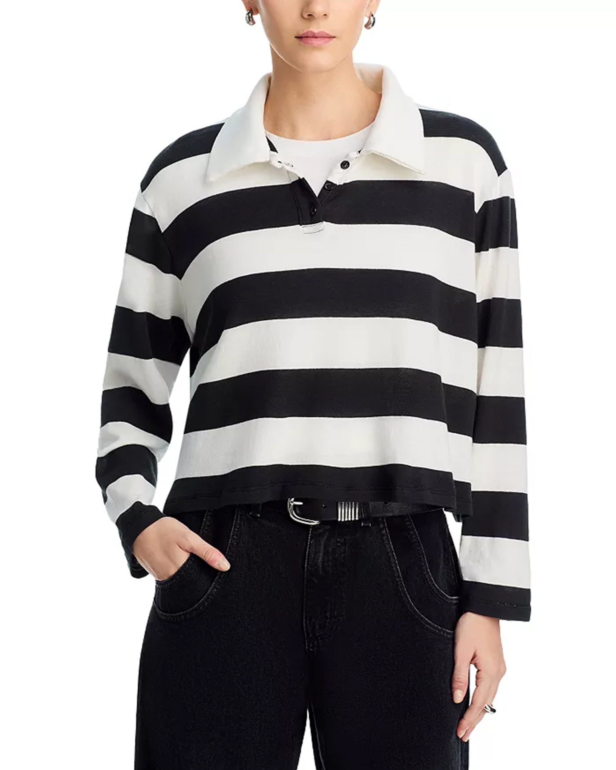 A person wearing the ASKK Long Sleeve Polo in black and white stripes, paired with black jeans and a black belt, stands with one hand in their pocket. The top of the head is partially cropped out of the image.