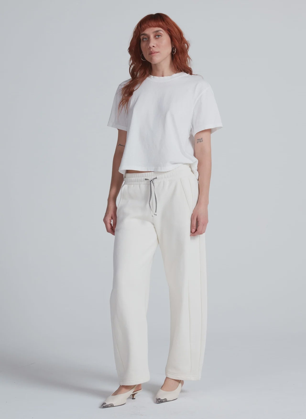 ASKK Cancun relaxed barrel sweatpants in white styled with tee and heels, minimal studio backdrop, modern look.
