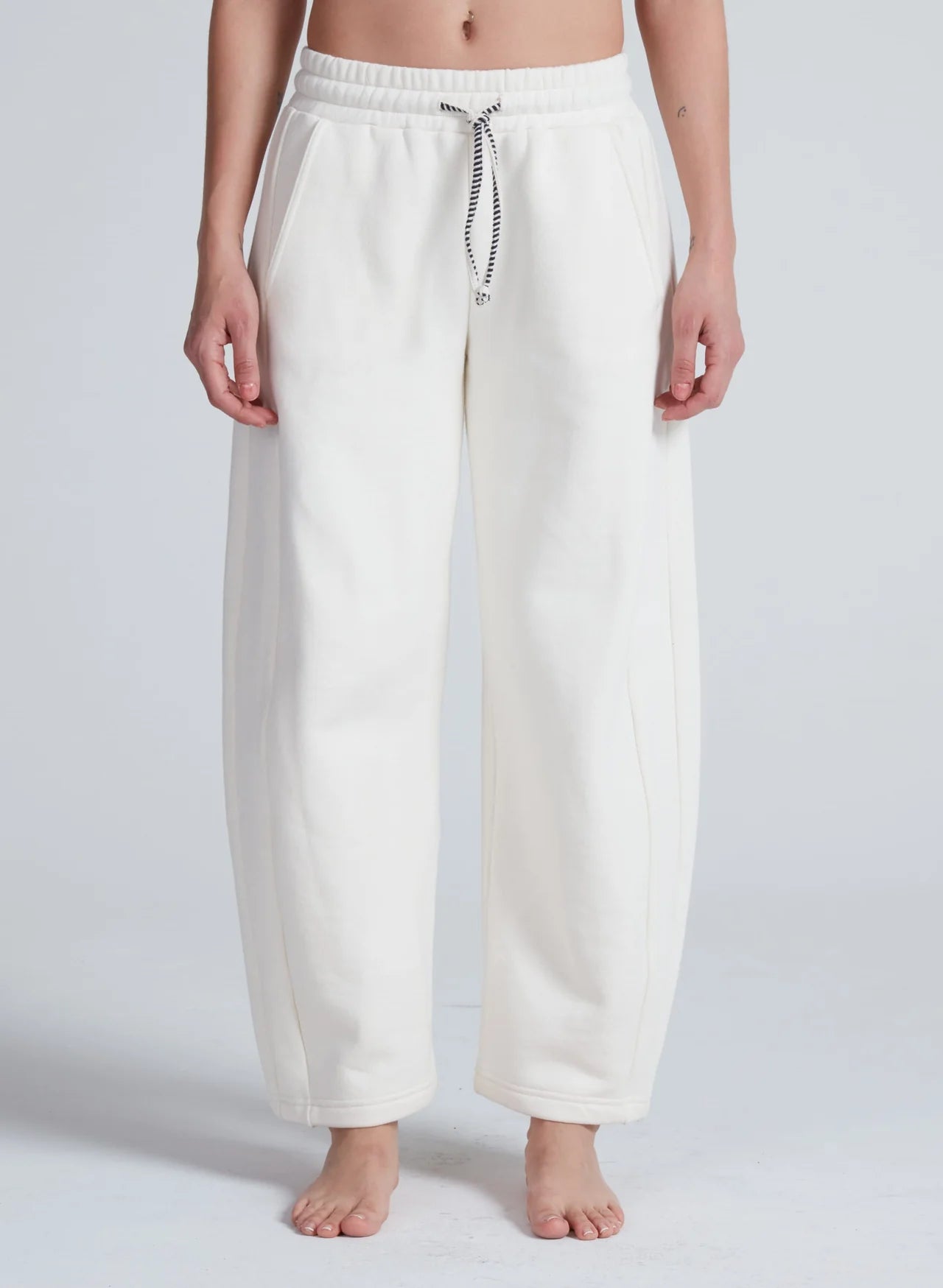 White ASKK Cancun Sweatpant with relaxed barrel fit, shown barefoot against a plain light background.