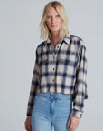 A woman with blonde, shoulder-length hair wears the ASKK Crosby Flannel in blue and white plaid, paired with light blue high-waisted jeans, standing against a plain light gray background.