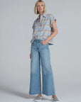 Wearing the ASKK Virginia Shirt, this person stands against a plain background in a relaxed pose with one hand in their pocket, paired with high-waisted wide-leg jeans and checkered slip-on sneakers.