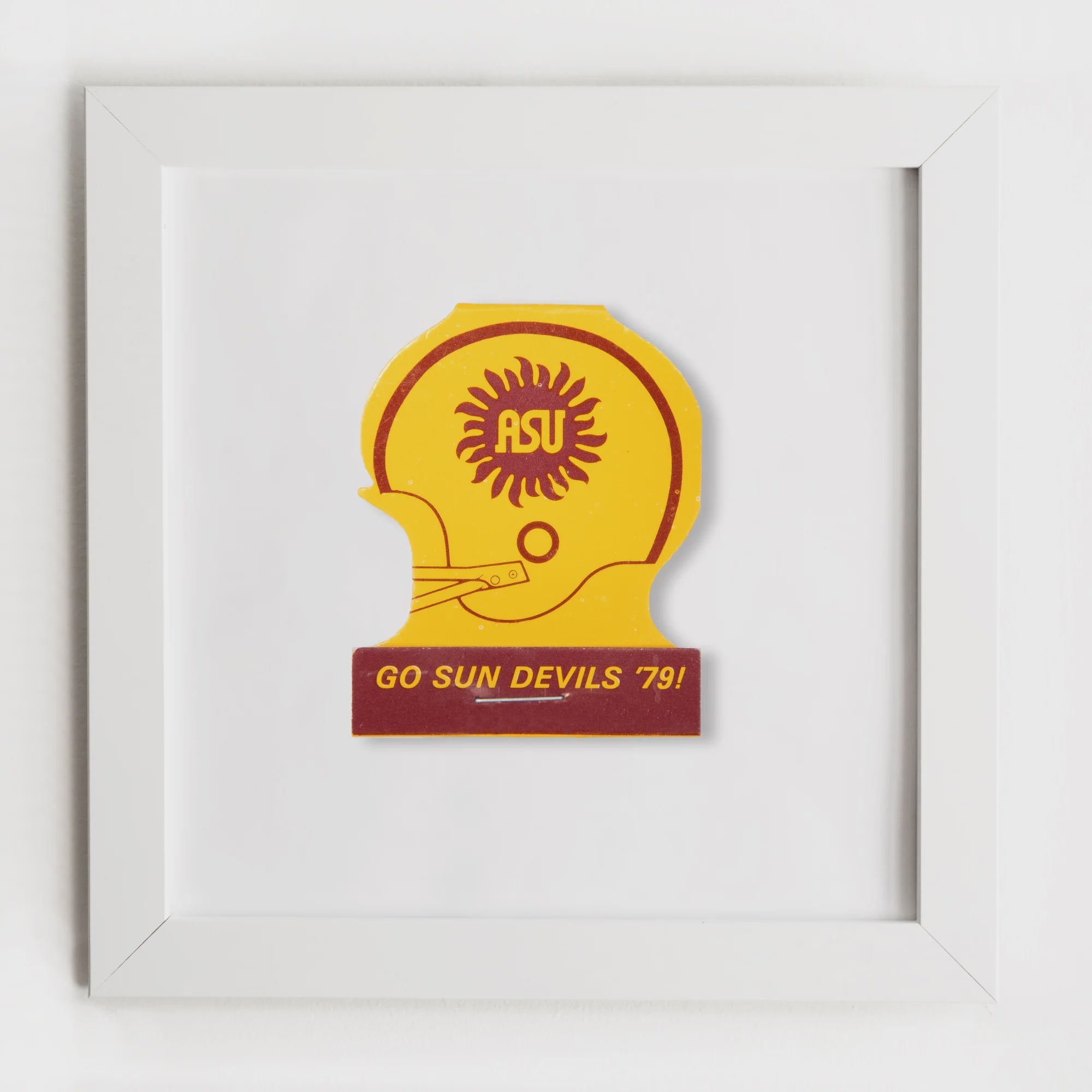 A Match South Art Square White Frame featuring a framed vintage Arizona State University sticker with a yellow and maroon design, the text &quot;Go Sun Devils &#39;79!&quot;, and a stylized sun motif in Bungalow style.