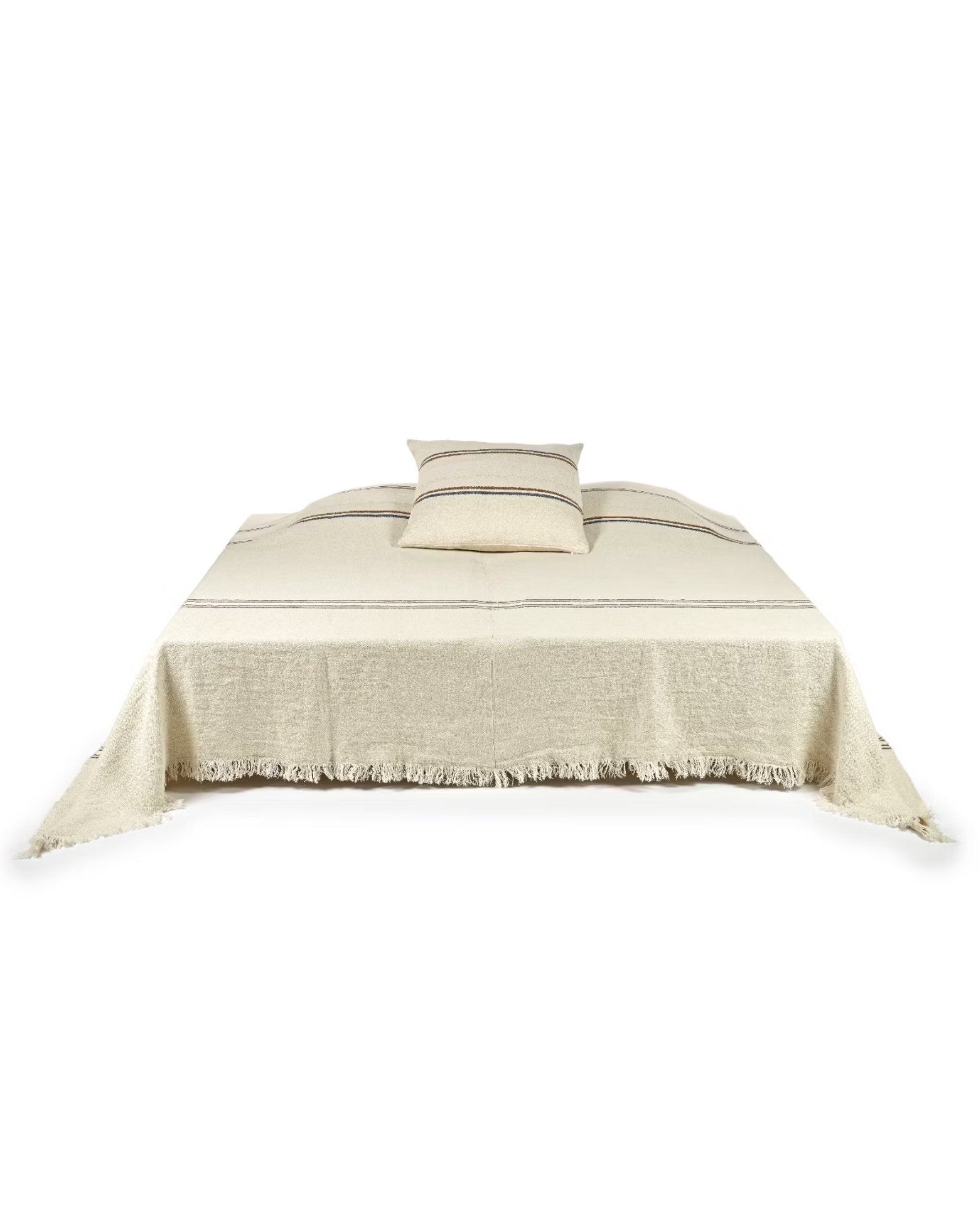 The Auburn Coverlet by Libeco Home, made of 100% linen in beige with subtle navy and bronze stripes and fringed edges, is displayed on a bed with a matching pillow against a white background.
