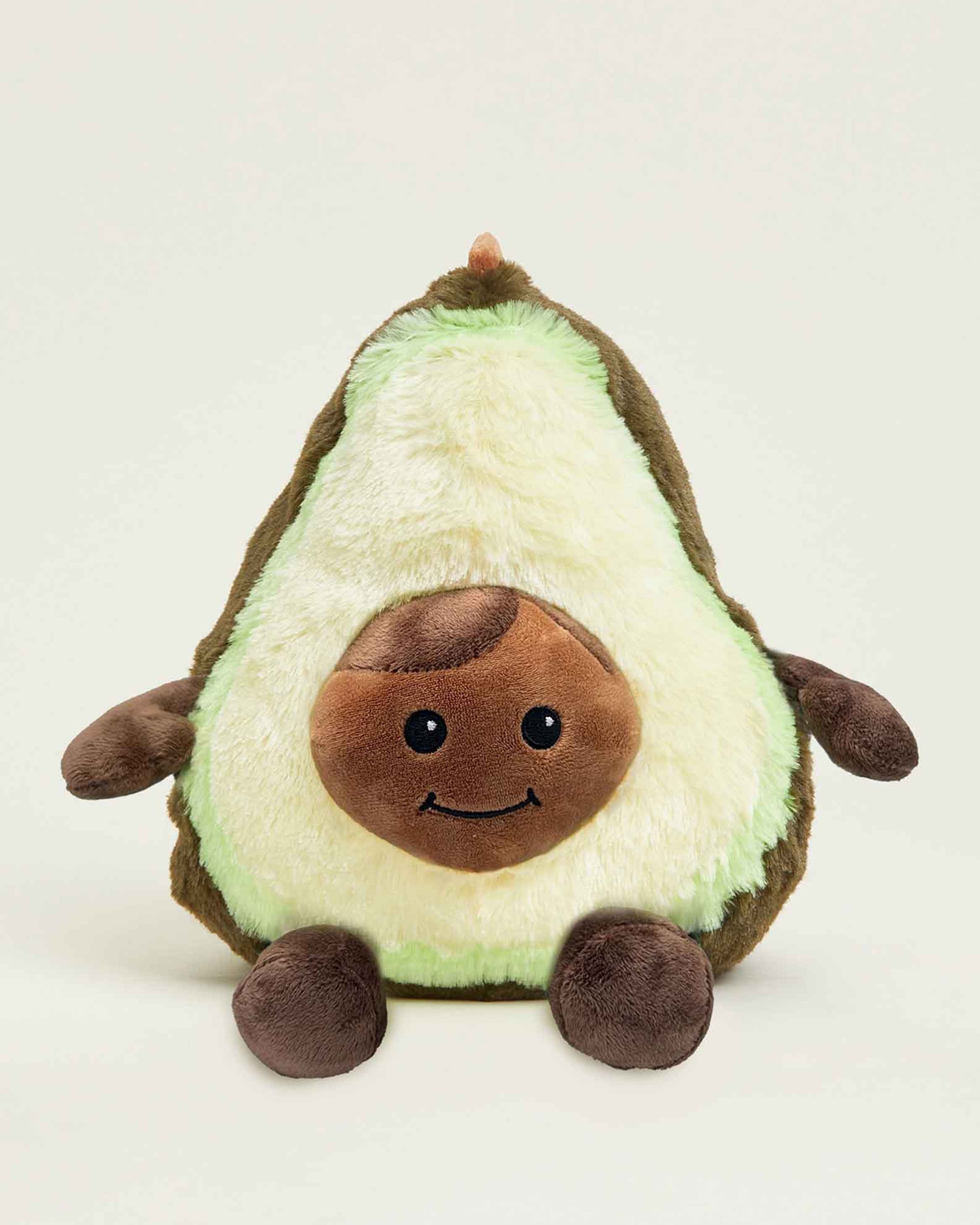 The Avocado Warmies by Faire is a microwavable plush toy shaped like a smiling avocado, featuring a light green center, dark green edge, brown pit, and cozy lavender scent. It sits upright against a plain background.
