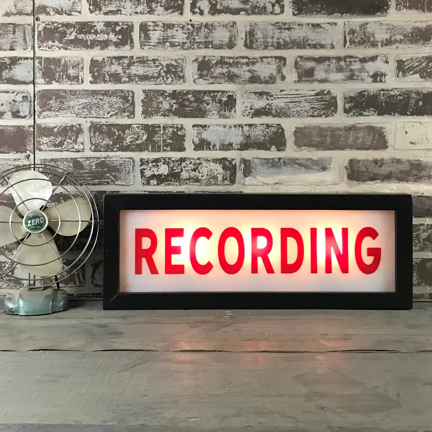 Faire's Lighted Sign features bold red "RECORDING" letters illuminated on a classic marquee, resting on wood near a vintage fan and brick wall—ideal personalized wall decor for creative spaces.
