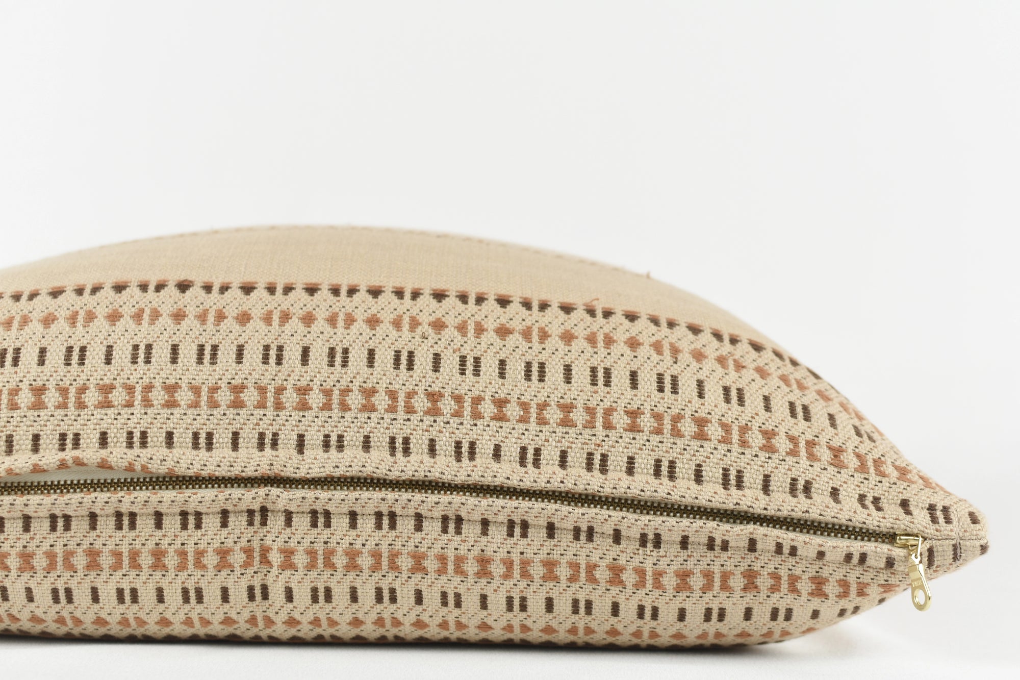 The Jacob Woven 22x22 Pillow by Faire features a beige cotton cover, handwoven in Gujarat, India, with a geometric brown and tan pattern and a gold zipper, shown partially open against a plain white background.