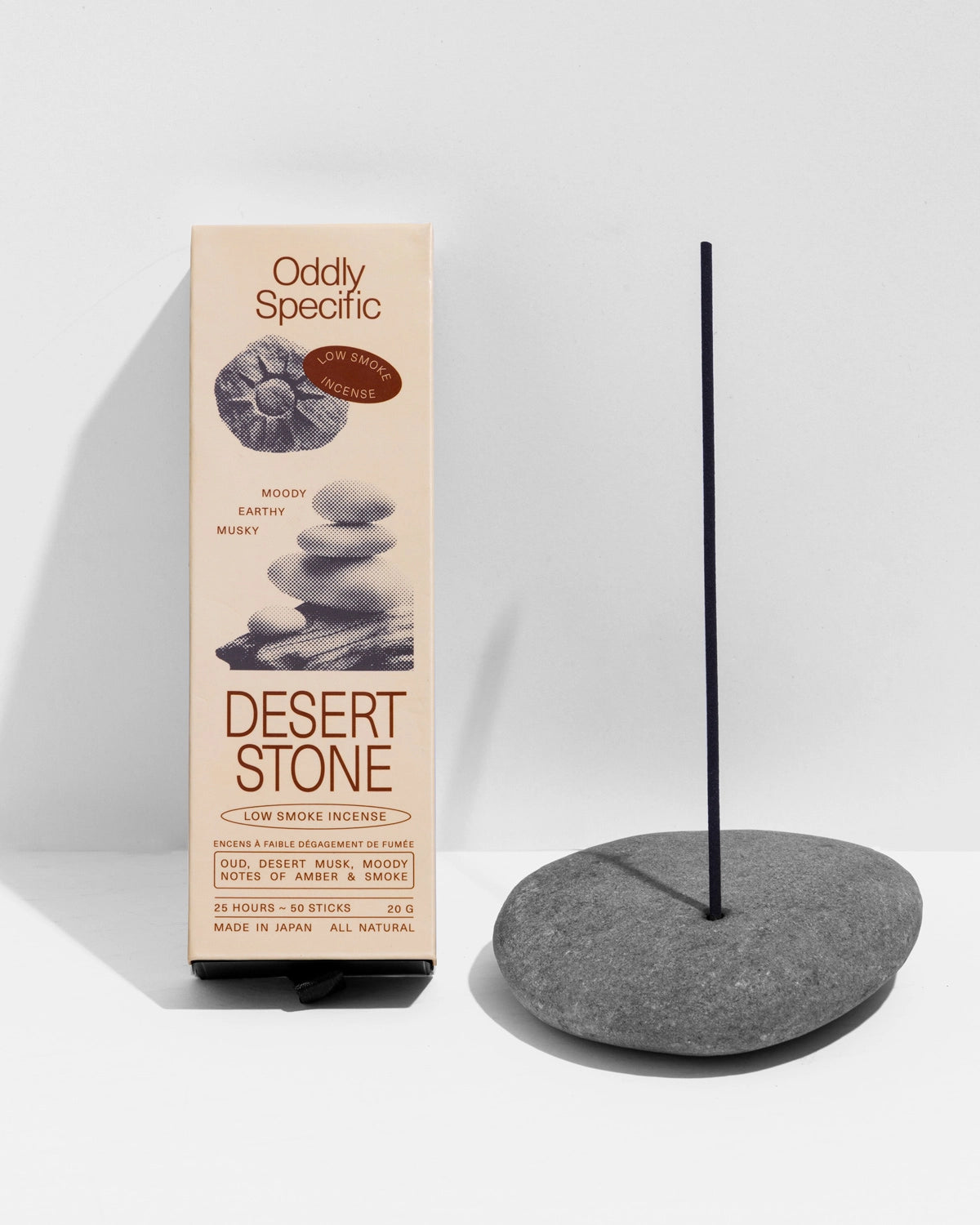 A box of Faire Low Smoke Incense stands next to a lit stick in a smooth gray stone holder against a white background. The beige packaging features stone graphics and product details.